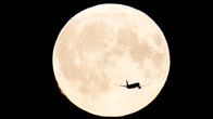 The silhouette of an airplane against the Moon.