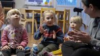 Kolme lasta istuu varhaiskasvatuspaikka Inarin kielipesässä lattialla. Vieressä istuu aikuinen, joka taputtaa käsiään yhteen.