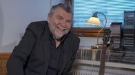 Kauko Röyhkä nauraa. Röyhkän vierellä kitara ja paljon cd-levyjä.