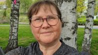 En kvinna med glasögon poserar framför en liten björkdunge.