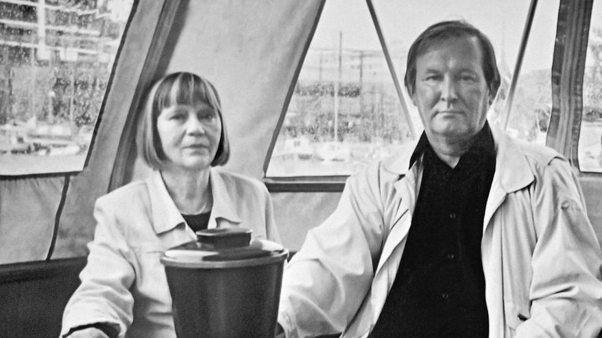Kuvassa mies ja nainen istuvat edessään tuhkakuppi ja uurna.