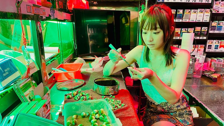 Nuori taiwanilaisnainen valmistelee betelpähkinöitä tiskillä vihertävissä neonvaloissa.