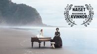 Nainen ja tyttö ja piano autiolla rannalla. Kuvassa iso Ohjaajina naiset -logo. Kuva elokuvasta Piano.