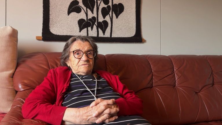 Ikäihminen Karoliina Nuorgam istuu sohvalla kotonaan Utsjoen Kaamasmukassa.