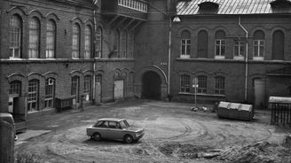 Vanha tiilinen tehdasrakennus, jonka keskellä pihalla on 1960-luvun henkilöauto. Taustalla näkyy tehtaan korkea savupiippu.