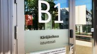 Talon ulko-ovi, jossa teksti B! ja sen alapuolella Käräjäoikeus istuntosali.