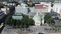 Ilmakuva torialueesta, jossa on vaalea kupolikattoinen rakennus, ympärillä puita ja taustalla liikerakennuksia.
