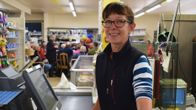 Åsa Storberg står i butikskassan, i bakgrunden en massa folk samlade runt ett bord.