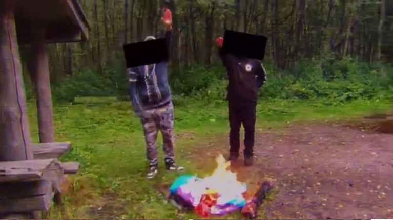 Kaksi uusnatsia tekee Hitler-tervehdyksen palavan pridelipun edessä. 