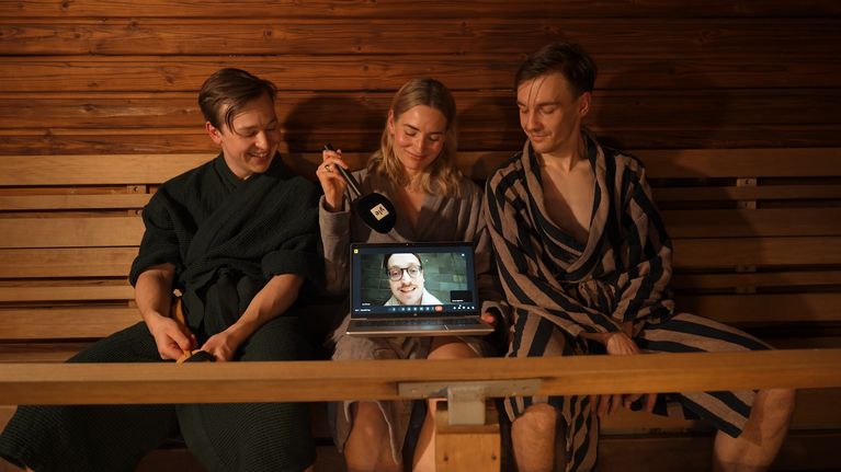 Två män och en kvinna i badrockar som tittar på en datorskärm med en bild på en man.