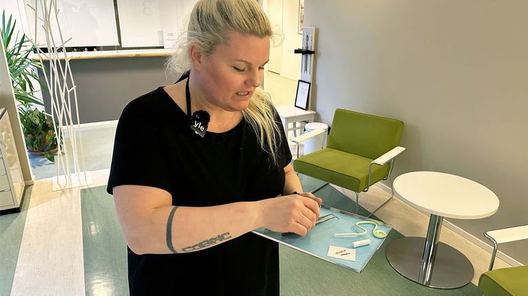 Nainen seisoo hammashoitolan vastaanottoaulassa ja pitelee kädessään metallista tarjotinta, jolle on aseteltu erilaisia hammashoidossa käytettäviä välineitä kuten poranteriä.