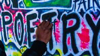 Käsi maalaamassa poetry -graffitia seinään.