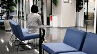 En kvinna sitter ensam på en blå soffa i en modern och sparsamt inredd vänthall eller lobby.