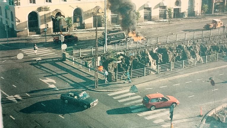 Ett fordon står i brand nära en byggnad med skylten "HOTELLI". Flera personer syns i området.