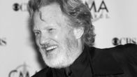 Mustavalkoinen kuva. Kris Kristofferson nauraa Country Music Awardsin punaisella matolla.