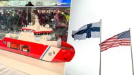 Pöydällä on lasikotelossa punavalkoisen laivan pienoismalli; taustalla Suomen ja Yhdysvaltain liput salossa.