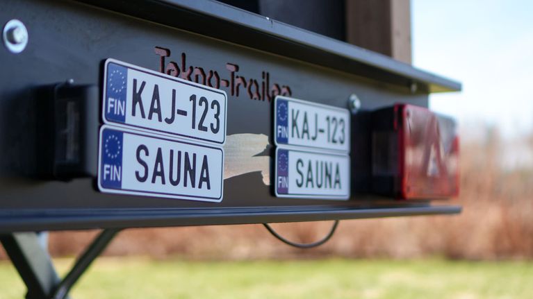 Peräkärrysaunan peräluukussa rekisterikyltit KAJ-123 ja SAUNA.