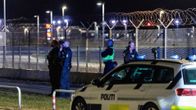 Useita poliiseja seisoo verkkoaidan vieressä lentoaseman kupeessa. Etualalla poliisiauto.
