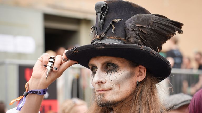 A long-haired man wearing gothic makeup and a black hat with a crow's wings and bones.