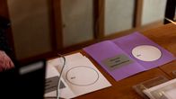 Äänestyspöytä, jossa on esillä valkoinen äänestyslipuke kuntavaaleihin ja violetti äänestyslipuke aluevaaleihin.