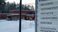 Kankaanpään terveyskeskuksen opastuskyltit, taustalla punainen tiilirakennus ja luminen talvimaisema.