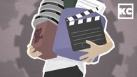Henkilö kantaa filmikeloja, klaffia, paperipinoa ja paljon muita kantamuksia