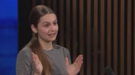 Ruskeahiuksinen tyttö puhuu. Hiukset ovat niskan takana poninhännällä. Vanessa Kovalenko A-studion haastattelussa.