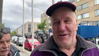 Vuolijokinen Veikko Haataja violetissa takissa ja lippalakissa Kajaanin kadulla, taustalla näkyy traktoreita ja perävaunuja.