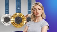 En kvinna med blont hår och ljusgrå t-skjorta tittar allvarligt in i kameran. I bakgrunden syns en bild på tre OS-medaljer: guld, silver och brons.