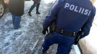 Poliisin sinisen haalarin selkä, kahden ihmisen jalat taustalla, jäinen maa. 