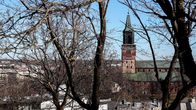 En röd stenkyrka syns bakom trädkronor.
