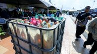 A large metal cart holding various plastic containers of different sizes. The containers hold used cooking oil which is intended to be refined into biofuels.