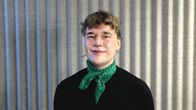 Mustaan paitaan ja vihreään huiviin pukeutunut nainen katsoo kameraan ja hymyilee.