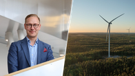 En person i blå kostym står inomhus; till höger syns ett vindkraftverk i ett skogsområde vid solnedgång.
