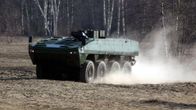 Kahdeksanrenkainen panssariajoneuvo liikkuu pellolla. Taustalla näkyy puita. 