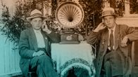 Kaksi nuorta miestä kuuntelee puutarhassa kannettavaa matkagramofonia noin 1920-luvun lopulla.