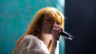 Florence + the Machinen solisti Florence Welch kasvot Flow-festivaalin lavalla. Laulaja laulaa ja pitää mikrofonia suunsa edessä. 