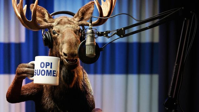 Tekoälyllä luotu fotorealistinen hirvi podcaststudiossa, muki kädessä. Mukissa lukee Opi suomea.