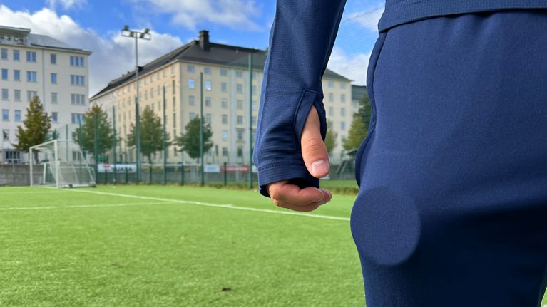 Henkilö seisoo jalkapallokentällä nuuskapurkki pullottamassa taskussa.