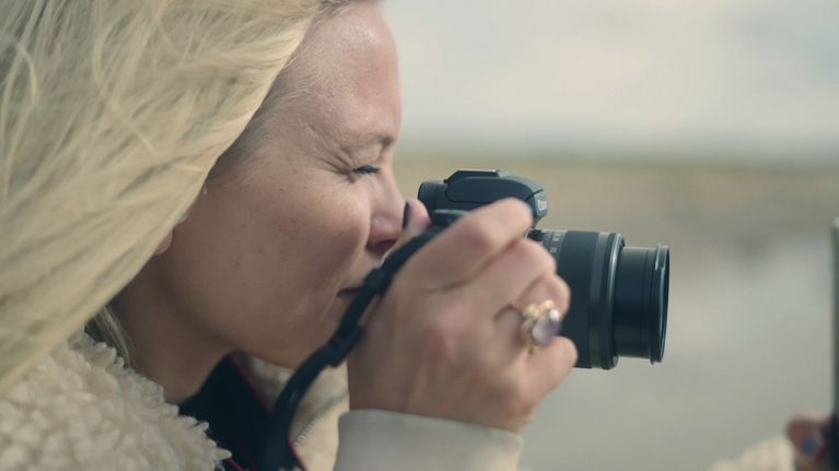 Emilia Hernesniemi lähikuvassa kamera kädessään. Hän katsoo etsintä ja siristää silmäänsä.