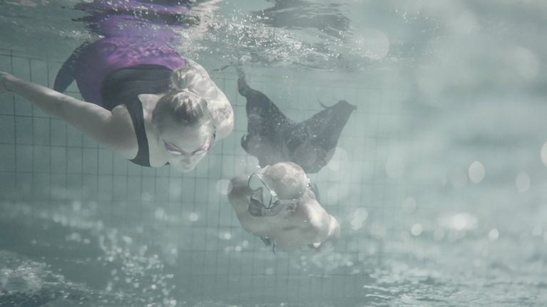 Vedenalaisessa kuvassa Emilia Hernesniemi ja Jani Toivola sukeltavat uima-altaassa merenneitopyrstöt yllään.