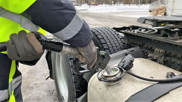 Huomiotakkiin ja työhanskoihin pukeutuneen ihmisen käsi, joka pitelee polttiainepistoolia isomman auton tankissa.