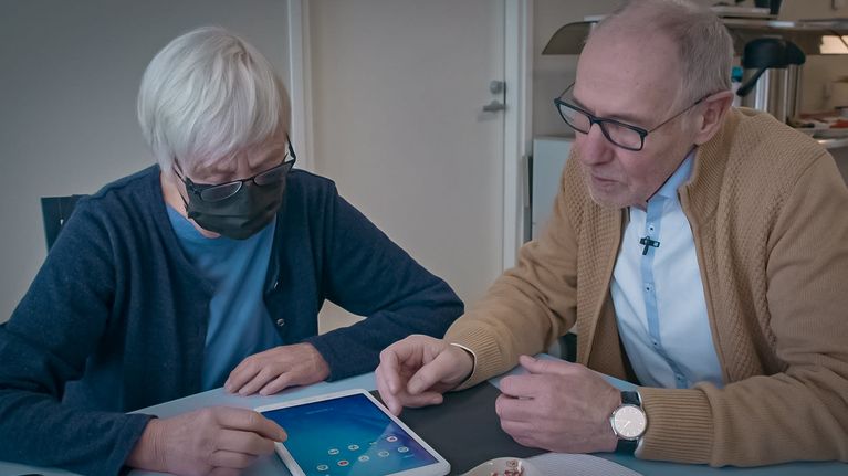Seniorinainen ja seniorimies ovat kumartuneet pöydällä tabletin äärelle.