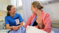 Mamma med bebis vid bröstet. Till höger om henne sitter en barnmorska.
