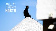 Photo shows a man sitting on the top of a stone structure.