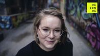 Bloggaaja Anna Giss katsoo hymyillen kameraan. Tautalla näkyy graffiteilla koristeltuja vanhojen tehdasrakennusten seiniä.