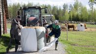 Två män jobbar med en höbal framför en traktor. 