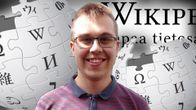 Tuomas Ahola katsoo kameraan ja taustalla Wikipedian logo