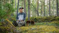 Panu Halme sitter i skogen med en svampkorg bredvid sig.