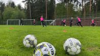 Kuvassa etualalla kolme jalkapalloa ja taaempana jalkapallojunioreita harjoituksissa.